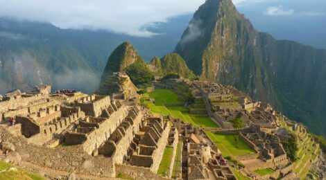 Aerial view of Machu Picchu’s ancient Inca citadel nestled in the Andes mountains with mist and lush landscape.
